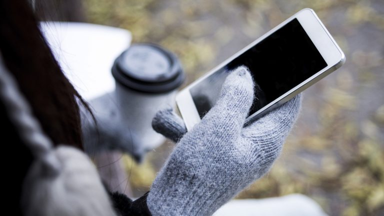 Handy im Winter draußen benutzen Eine Person mit Handschuhen hält ein Smartphone in der Hand.