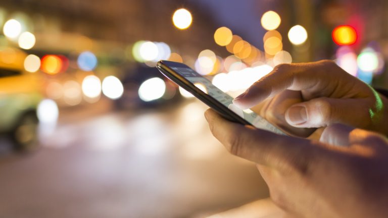Männerhände mit iPhone vor regem Straßentreiben