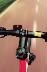 Fahrradfahrer stützt Hand auf Lenker, um Smartphone zu bedienen.