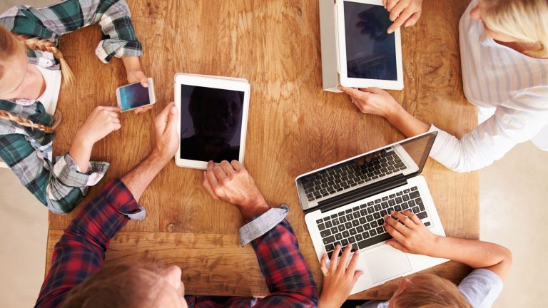 Familie mit Apple-Geräten am Tisch nutzt Apple-Familienfreigabe