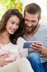 Eltern mit Kleinkind und Smartphone auf einem Sofa
