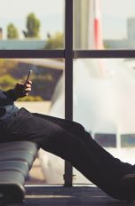 Ein Mann mit Bügel-Kopfhörern sitzt am Terminal auf den Sitzen und schaut aufs Smartphone