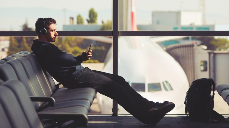 Ein Mann mit Bügel-Kopfhörern sitzt am Terminal auf den Sitzen und schaut aufs Smartphone
