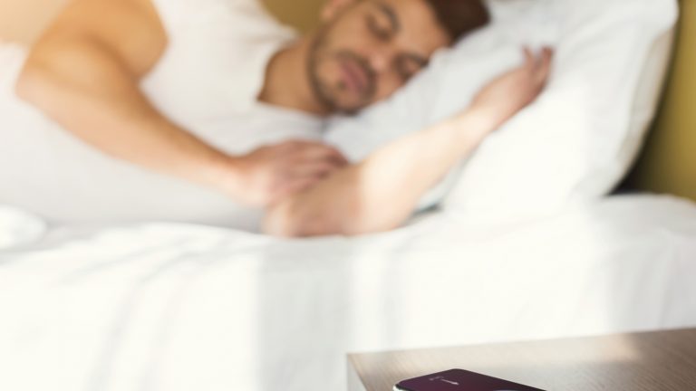 Smartphone liegt auf dem Nachtisch und überwacht den Schlaf eines Mannes Smartphone liegt auf dem Nachtisch und überwacht den Schlaf eines Mannes