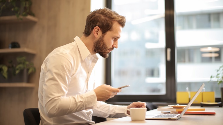 Mann mit Smartphone am Laptop