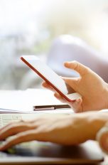 Person sitzt am Tisch und schaut aufs Smartphone
