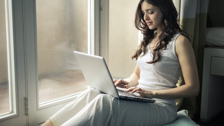 Frau am Fenster sitzend surft am Notebook Frau am Fenster sitzend surft am Notebook