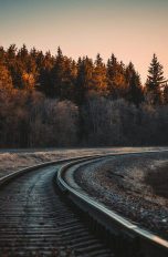 Bahn-Schinen führen in einer Rechtskurve in den Sonnenuntergang. Drum herum sind Bäume.