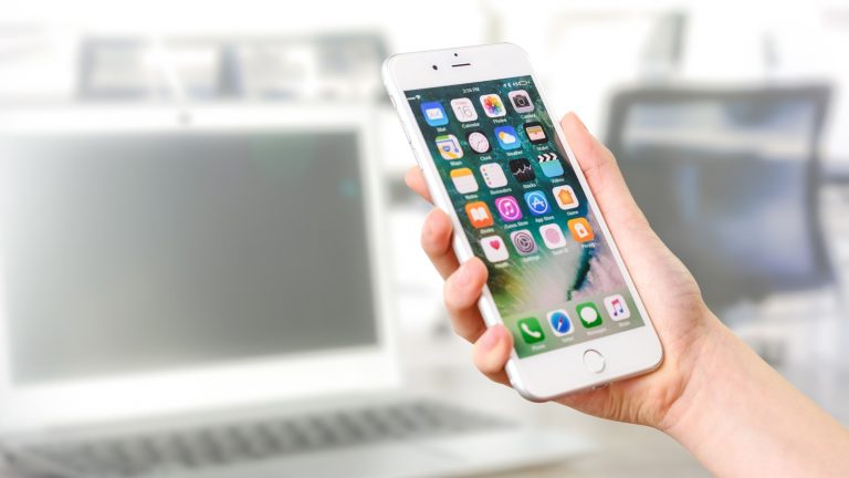 iPhone in der Hand vor einem MacBook iPhone in der Hand vor einem MacBook