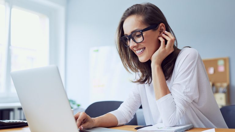 Windows 10 Sprache ändern: Frau sitzt am Laptop und lächelt