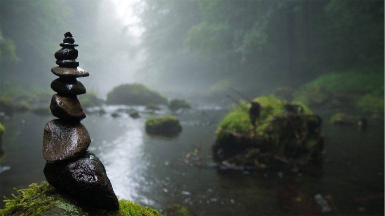 Gestapelte Steine an einem Flussufer vor nebligem Wald