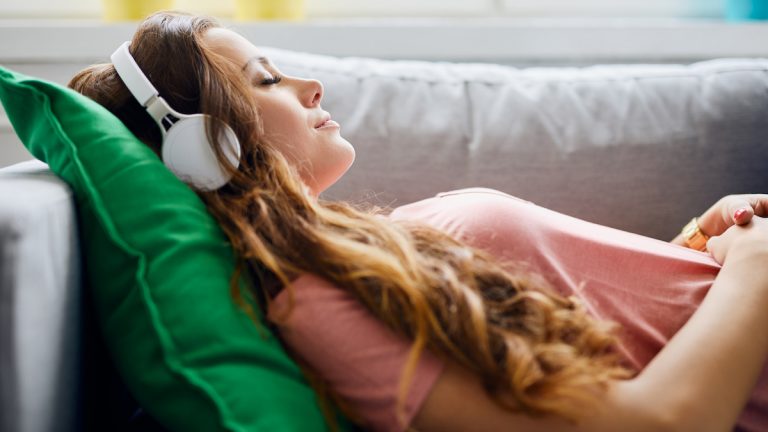 Attraktive Frau liegt auf dem Sofa und hört ein Hörbuch
