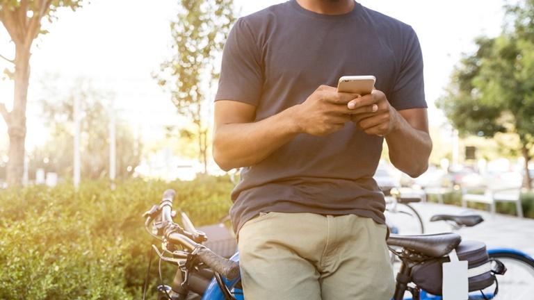 Mann mit Smartphone lehnt an Fahrradständer