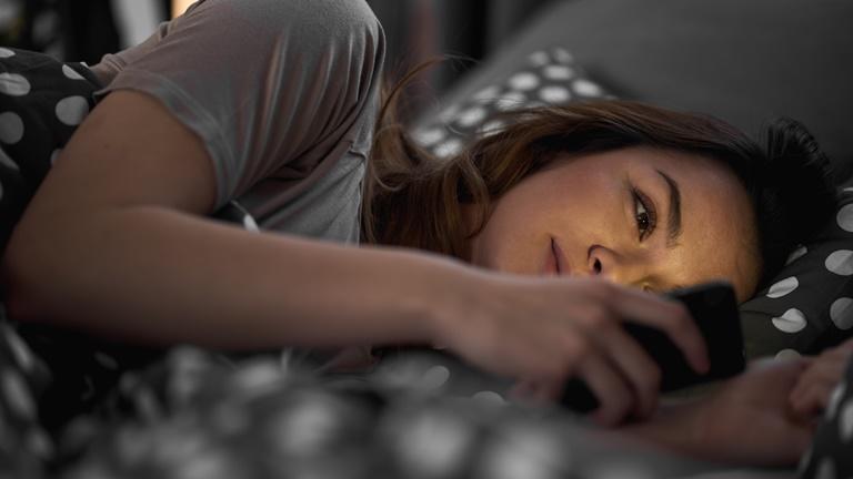 Frau liegt im Bett und sieht auf Smartphone mit gelblichem Licht Frau liegt im Bett und sieht auf Smartphone mit gelblichem Licht