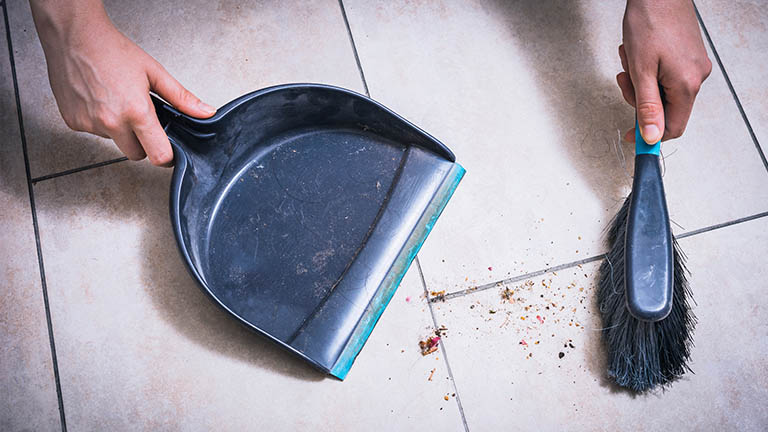 Großreinemachen: Mit Akkubesen oder Staubsauger? Person reinigt mit Kehrschaufel und Handfeger Fliesen