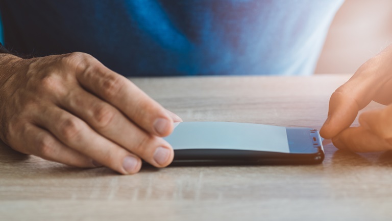 Mann bringt Schutzfolie auf Smartphone Display an Mann bringt Schutzfolie auf Smartphone Display an