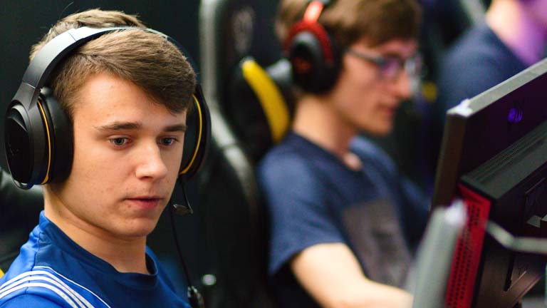 Zwei junge Männer spielen an zwei PS4 und tragen dabei ein Headset