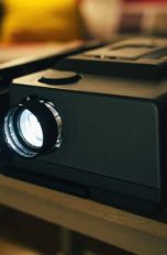 Älterer Heimkino-Beamer steht eingeschaltet auf Wohnzimmertisch