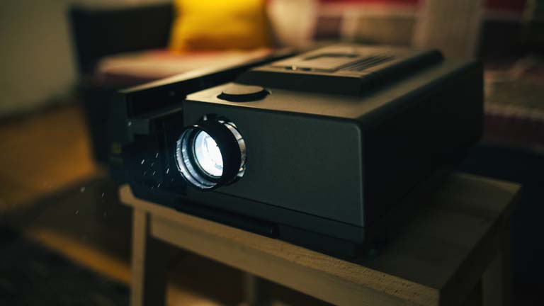 Älterer Heimkino-Beamer steht eingeschaltet auf Wohnzimmertisch