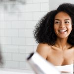 Junge Frau lächelt und föhnt sich mit einem Reiseföhn die Haare