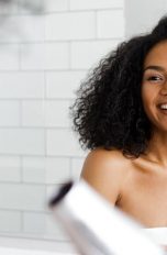 Junge Frau lächelt und föhnt sich mit einem Reiseföhn die Haare