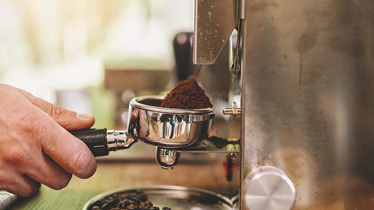 Hand hält Siebträger, frisch gemahlenes Kaffeepulver rieselt hinein