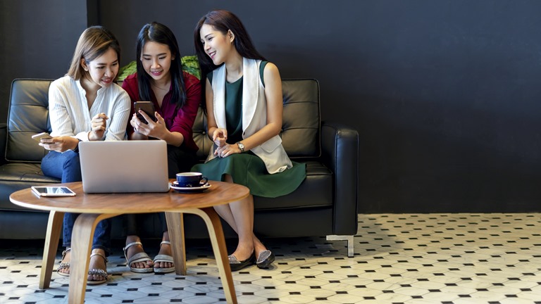 Freundinnen sitzen im Cafe und schauen auf Smartphone und Laptop
