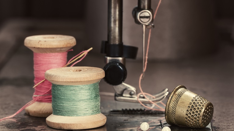 Nähmaschine kaputt? So kannst du deine Nähmaschine selbst reparieren Buntes Garn und ein Fingerhut neben der Nadel einer Nähmaschine