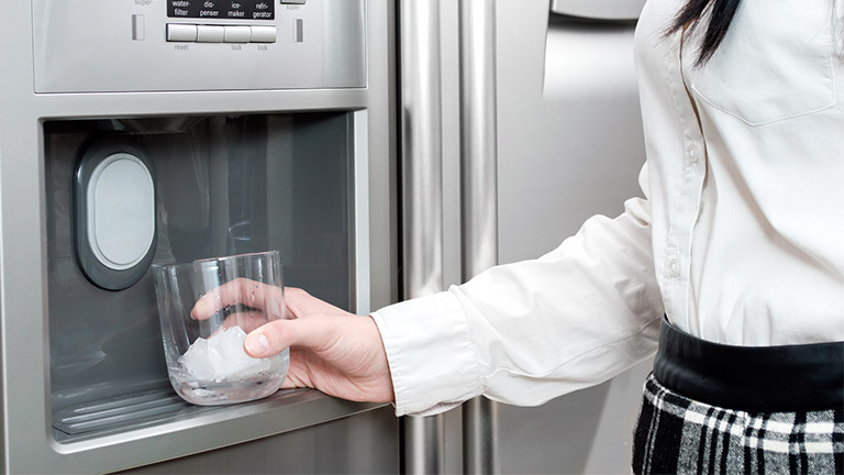 Side-by-Side Kühlschrank mit Eiswürfelmaschine: Wassertank oder Festwasseranschluss? Eine Frau nutzt den Side-by-Side-Kühlschrank, um sich im Sommer mit Eiswürfeln abzukühlen