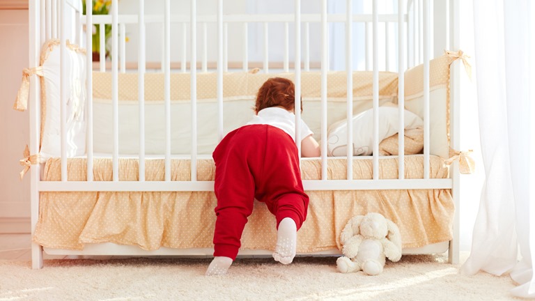 Kleines Kind klettert aus dem Gitterbett 