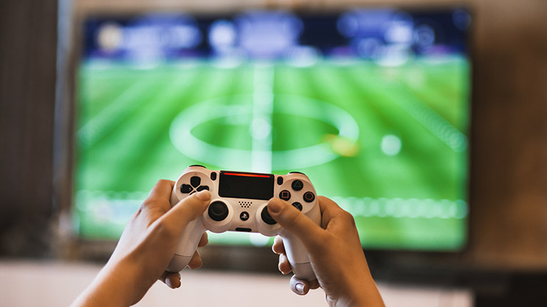 7 PS4-Tipps für mehr Spielspaß mit deiner Konsole Weißer Dualshock-Controller für die PS4 mit Sport-Game im Hintergrund