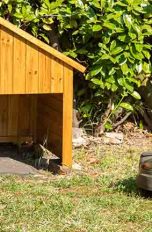 Ein Mähroboter fährt über eine Wiese. Am Rand stehen Hecken und Büsche. Davor steht eine Garage mit integrierter Ladestation für den Mähroboter.