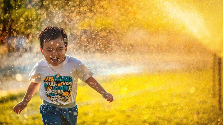 Junge läuft lachend durch Sommerregen