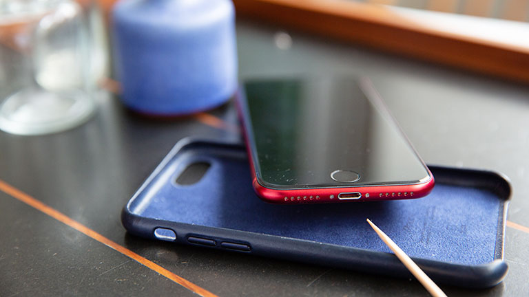 Smartphone desinfizieren Ein Zahnstocher deutet die Reinigung der Lautsprecher-Öffnungen am iPhone SE an. Unter dem Smartphone liegt eine Hülle.