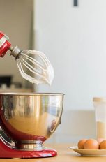 Ein Mixer von KitchenAid steht neben ein paar Eiern auf einem Küchentisch.