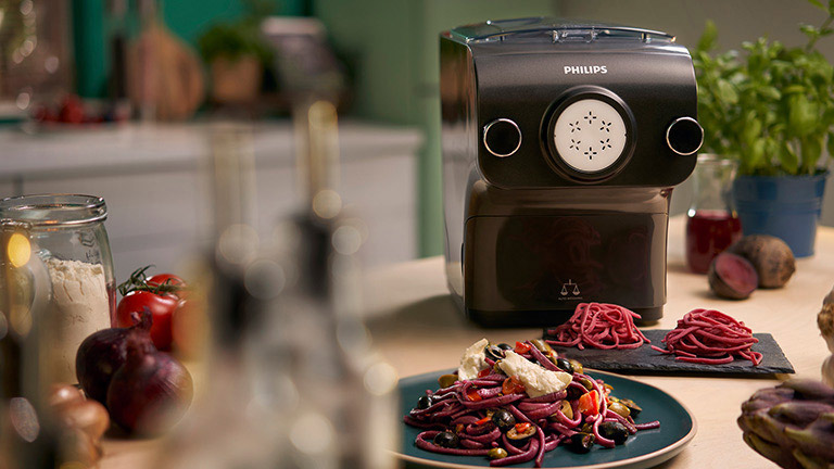 philips avance collection pastamaker hr2382 Die Nudelmaschine von Philips steht auf einem Küchentisch, davor zwei Teller mit fertig angerichteter Pasta.