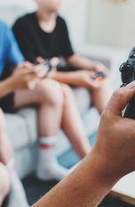 Mehrere Personen sitzen in einem Zimmer und haben PS4-Controller in der Hand.