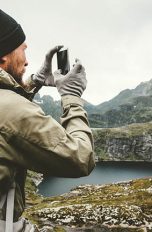 Ein Wanderer steht vor einem Berg. Mit seinem Smartphone nimmt er ein Bild der Szenerie auf.