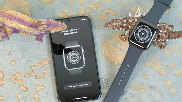 Apple Watch 5 Apple Watch und iPhone liegen neben zwei Spielzeug-Dinosauriern nebeneinander. Auf den Display ist zu sehen, dass die Kopplung der Apple Watch erfolgreich war.