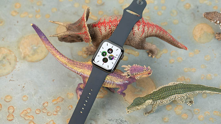 Apple Watch 5 Die Apple Watch liegt auf Spielzeug-Dinosaurieren. Auf dem Display lässt sich ein weißes Ziffernblatt erkennen.