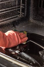 Eine Person mit Handschuhen wischt mit einem Schwamm den Backofen aus.