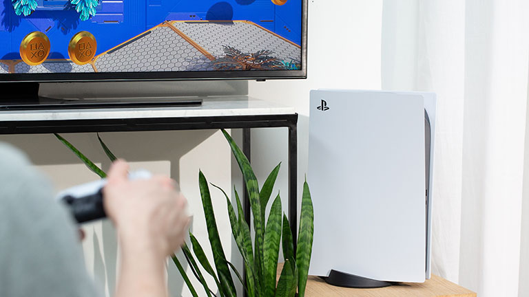 Playstation 5 Die PlayStation 5 steht aufrecht leicht rechts unterhalb eines Fernsehers.