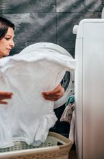 Eine Person holt ein weißes Kleidungsstück aus einem Trockner.