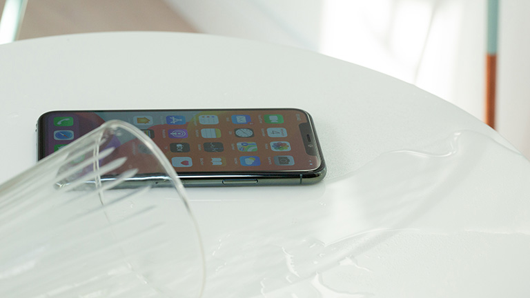iPhone 11 Ein verschüttetes Glas Wasser. Die Flüssigkeit fließt an einem iPhone 11 vorbei.