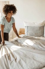 Eine Person macht ihr Bett. Die Bettäsche ist Grau-Weiß.