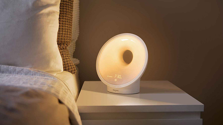 Tageslichtlampe Der Tageslichtwecker Philips Somneo auf dem Nachttisch neben einem Bett.