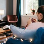 Eine Person sitzt auf dem Sofa und strickt. Nebenbei sieht sie fern.