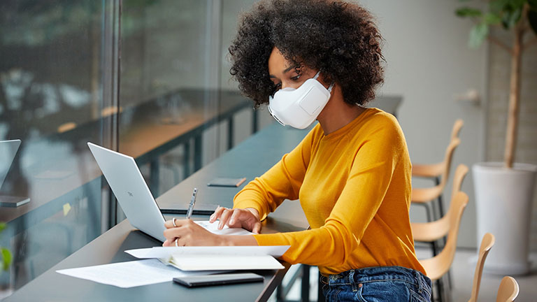 Eine Person trägt die PuriCare-Maske von LG, während sie in einem Büro am Laptop arbeitet.