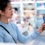 Eine Person hält ihr Smartphone mit Payback Pay in Richtung einer Kasse.