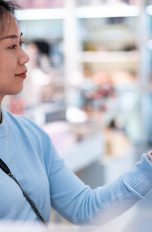 Eine Person hält ihr Smartphone mit Payback Pay in Richtung einer Kasse.